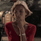 a woman in a red shirt is smoking a cigarette while wearing a watch on her wrist