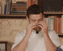 a man in a white shirt is covering his nose with his hands