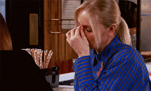 a woman in a blue striped shirt is covering her nose with her hands