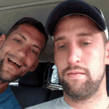 two men are posing for a picture with one wearing a baseball cap