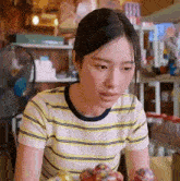 a woman in a yellow and white striped shirt is sitting at a table in a room .