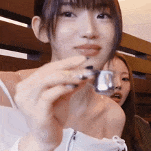 two young women are sitting next to each other and one is holding a small object in her hand .