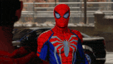 a man in a red and blue spiderman costume stands next to a car