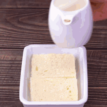slices of bread are being poured into a white casserole dish