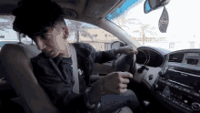 a man is driving a car with an air freshener hanging from the rearview mirror