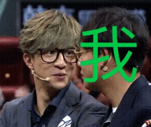 a man wearing glasses and a microphone talks to another man with a green chinese symbol on his face