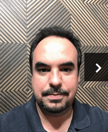 a man with a beard is standing in front of a wall with a diagonal pattern