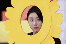 a woman wearing a microphone looks out of a hole in a yellow circle