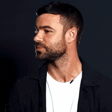 a man with a beard is wearing a black jacket and a white t-shirt