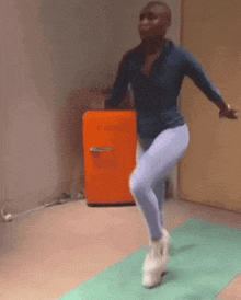 a man is jumping on a yoga mat in front of an orange refrigerator .