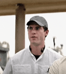 a man wearing a baseball cap and a white shirt is standing next to a wooden post .