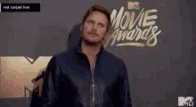 a man in a black jacket is standing in front of a red carpet at the movie awards .