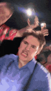 a man in a blue shirt is making a funny face while being photographed by another man .
