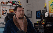 a man wearing a robe is sitting in a chair in front of a cuphead poster .