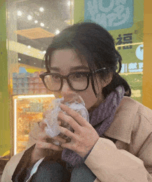 a woman wearing glasses eating a sandwich in front of a store that says now happy