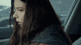 a woman with long dark hair is sitting in the back seat of a car