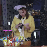 a woman in a yellow sweater is standing in front of a basket of snacks including a bag of oreos