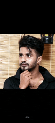 a man with a beard and mustache is wearing a black shirt and a gold chain around his neck
