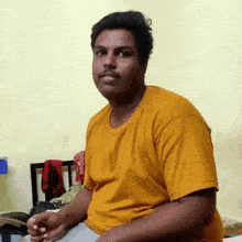 a man in a yellow shirt is sitting on a bed making a funny face