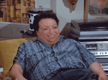 a woman in a blue shirt is smiling while sitting on a couch in front of a record player