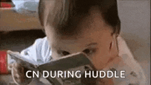 a baby is reading a book with the words `` cn during huddle '' above it .