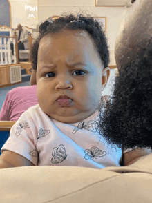 a baby wearing a pink shirt with butterflies on it making a funny face