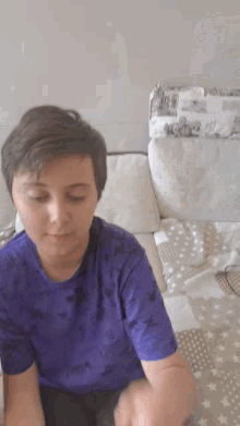 a young boy in a purple shirt is sitting on a couch with his eyes closed