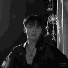 a black and white photo of a young man with a dream catcher behind him