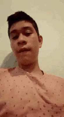 a young man in a pink shirt is making a funny face while looking at the camera .