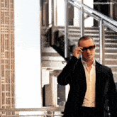 a man wearing sunglasses and a suit is walking down stairs