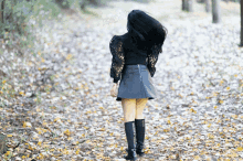 a woman in a black skirt and black boots is walking through a forest