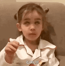 a little girl is sitting on a couch eating a piece of cake and making a funny face .