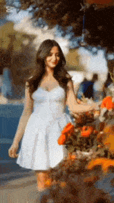 a woman in a white dress is standing in front of a row of flowers .