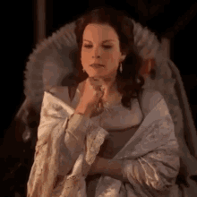 a woman in a costume is sitting in a chair with her hand to her chin .