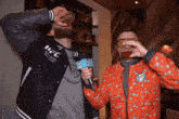 a man wearing a ufc jacket is drinking from a glass