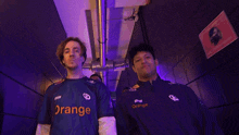 a man in an orange shirt stands next to another man in a blue shirt