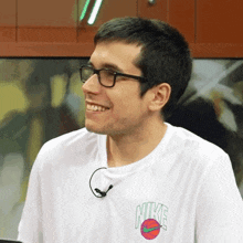 a man wearing glasses and a nike t-shirt smiles