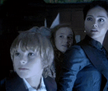a woman in a blue jacket stands between two children
