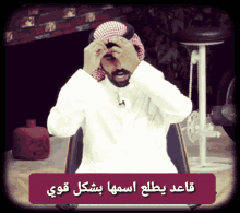 a man wearing a turban is sitting in front of a sign that says " قاعد يطلع اسمها بشكل قوى "