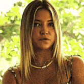 a woman wearing a green dress and a necklace is standing in front of a tree .