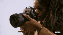 a woman is taking a picture with a camera with the bet logo in the corner