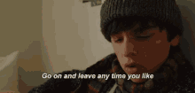 a young boy wearing a beanie and a scarf is sitting in a room and talking .