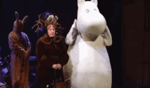 a woman in a brown coat is standing next to a white stuffed animal .