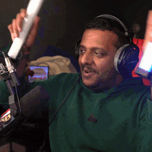 a man wearing headphones and a green sweatshirt holds up two red lightsabers