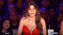a woman in a red dress is sitting in front of a microphone with a nbc logo in the background