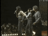 three men singing into microphones in front of a crowd