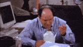 a bald man is sitting at a desk eating a box of food .