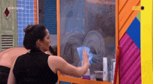 a woman in a black tank top is cleaning a glass door with a blue cloth .