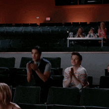 a group of people applauding in an auditorium with a red exit sign in the background