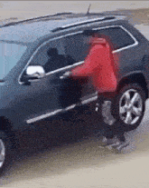 a man in a red jacket is trying to get into a car .